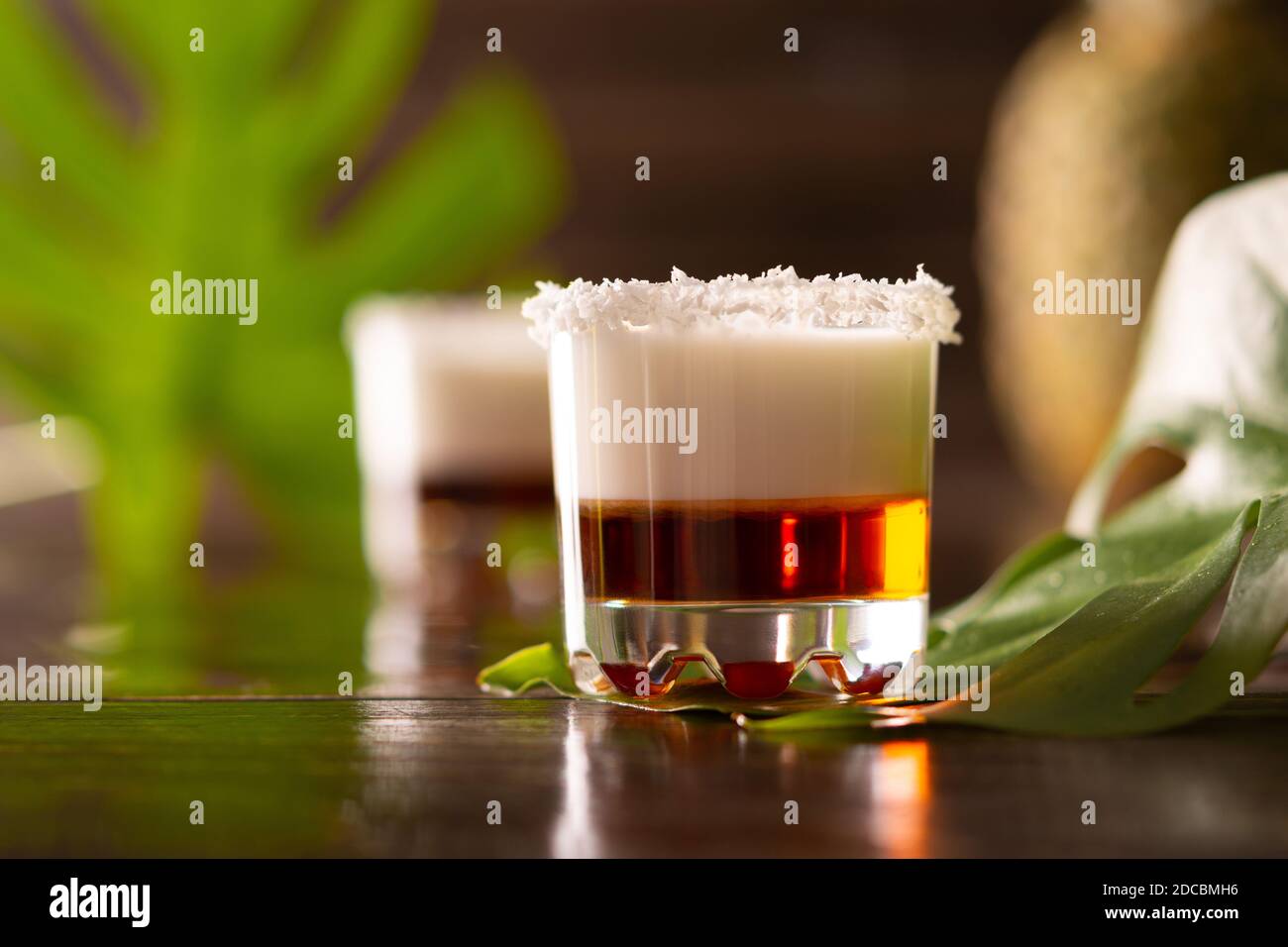 Tropische alkoholische Aufnahmen mit Kokosflocken, Monstera Blume mit Kokosnuss und Ananas auf braunem Holzhintergrund dekoriert Stockfoto