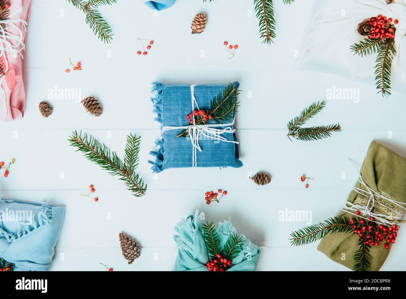 Draufsicht Zero Waste weihnachtskonzept. Geschenkschachteln in Stoff mit Fichtenzweig und roten Beeren auf weißem Holzhintergrund mit natürlichen verpackt Stockfoto