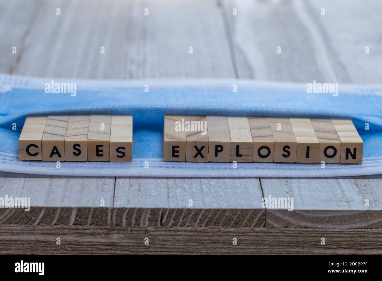 EXPLOSION von Fällen auf Gesichtsmaske covid Pandemiealarm Konzept Holzblock Buchstaben an Bord kühlen blauen Ton Hintergrund Stockfoto