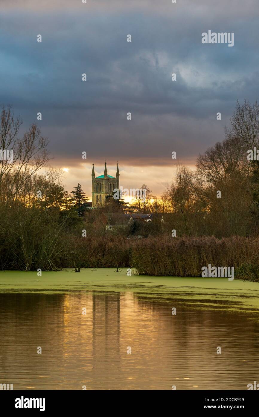 Ein Winterblick auf Pershore Abbey über den See bei Avon Meadows Wetland Reserve bei Sonnenuntergang, Worcestershire, England Stockfoto