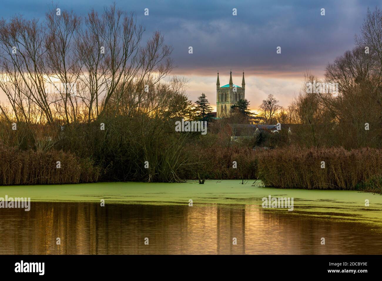 Ein Winterblick auf Pershore Abbey über den See bei Avon Meadows Wetland Reserve bei Sonnenuntergang, Worcestershire, England Stockfoto