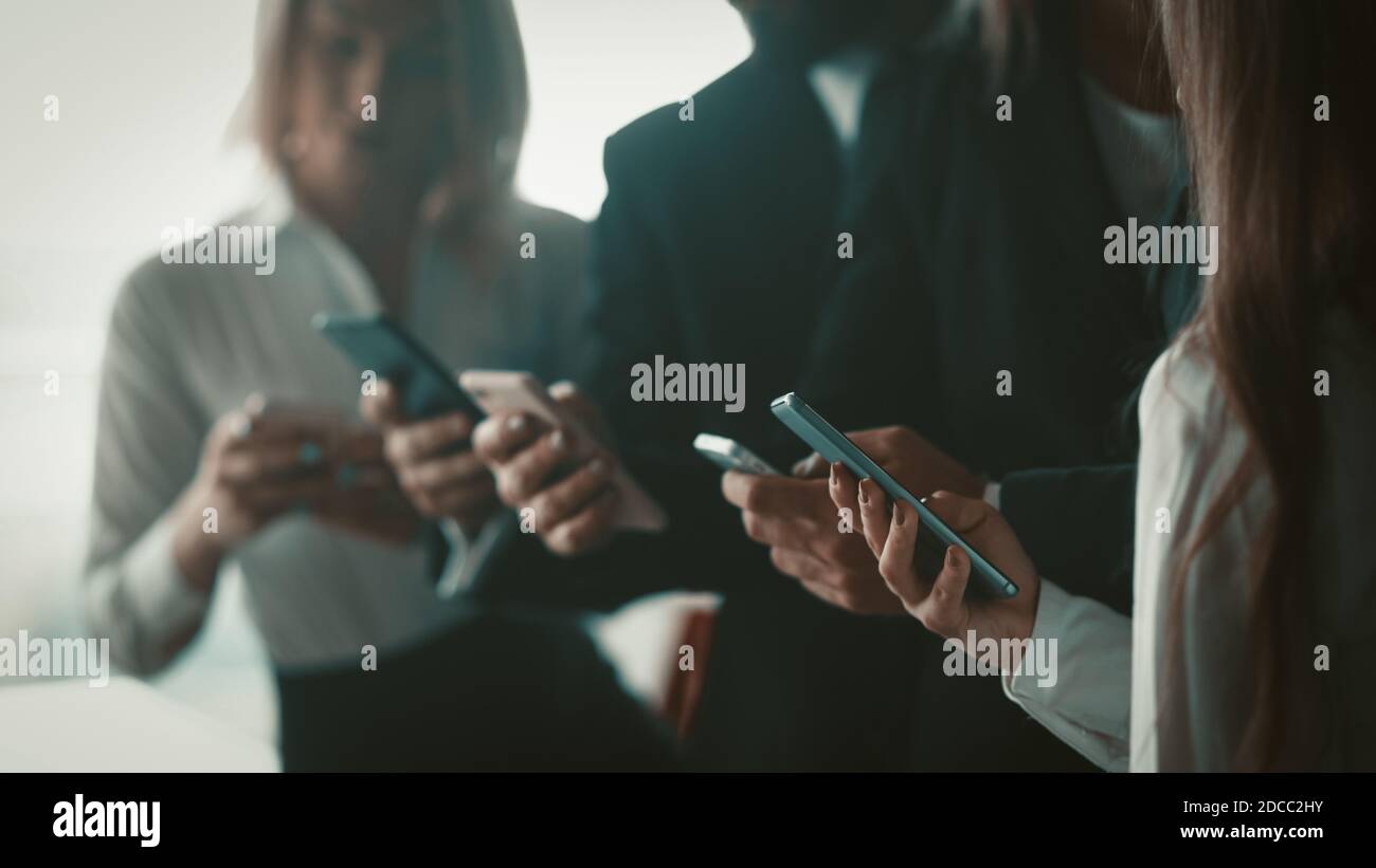 Geschäftsleute, die gemeinsam Mobiltelefone nutzen, stehen im Büro. Nahaufnahme von menschlichen Händen, die Smartphones halten. Verschwommenes Bild. Selektiver Fokus auf Stockfoto