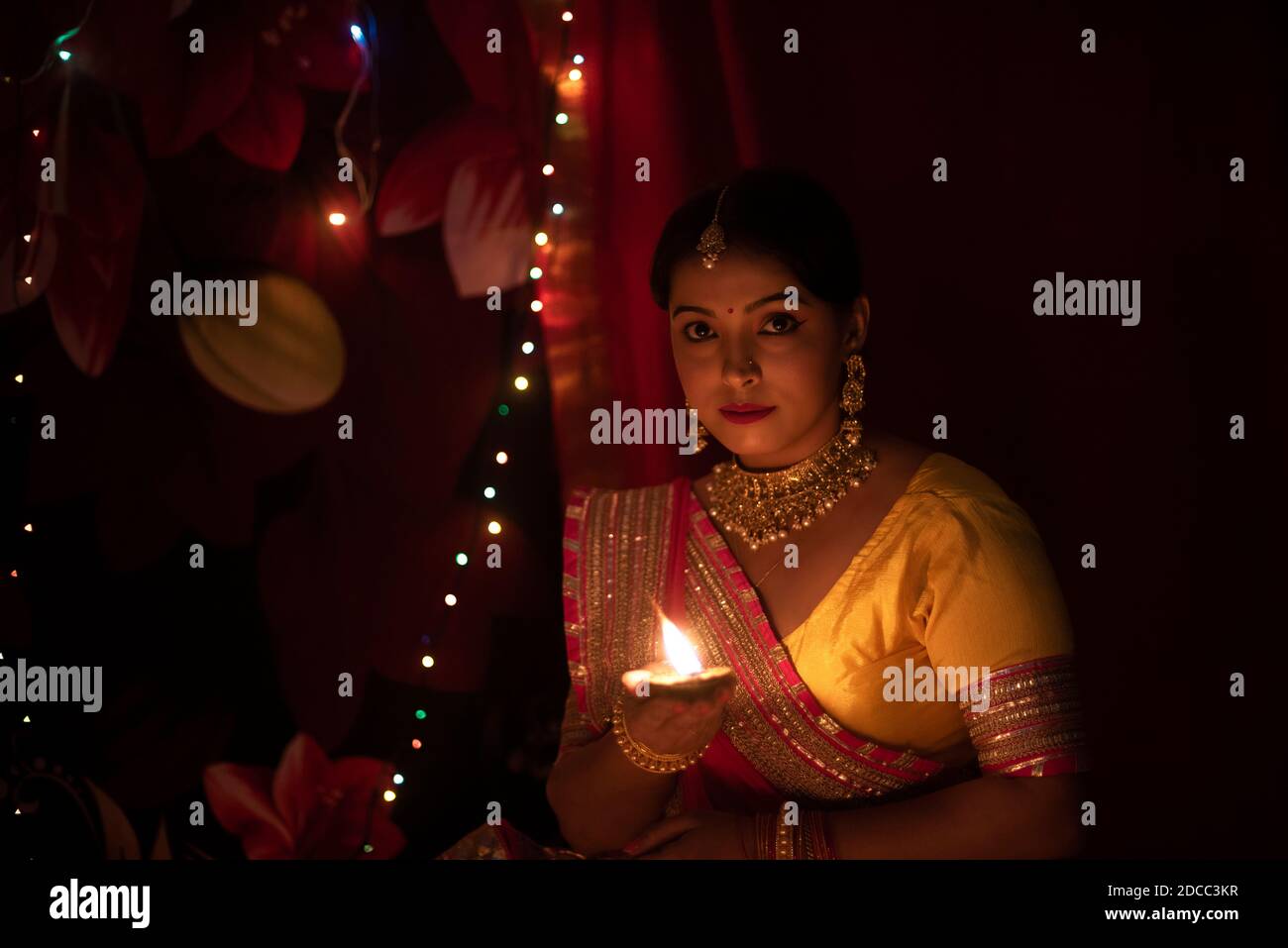 Eine junge und schöne indische Bengalin in indischer Tracht hält eine Diwali diya/Lampe in der Hand vor bunten Bokeh-Lichtern. ICH Stockfoto