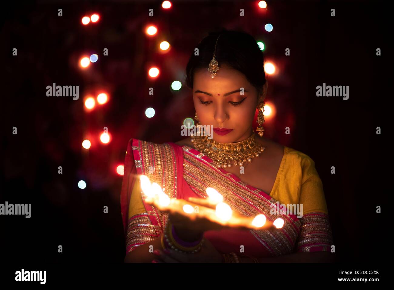 Eine junge und schöne indische Bengalin in indischer Tracht hält eine Diwali diya/Lampe in der Hand vor bunten Bokeh-Lichtern. ICH Stockfoto