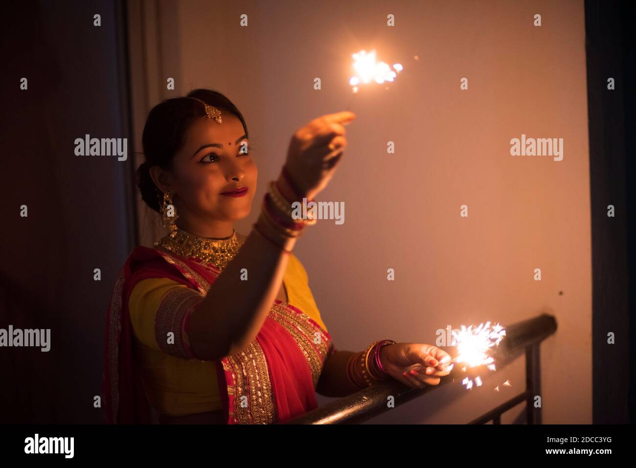Junge und schöne indische Bengali Frau in indischen traditionellen Kleid feiert Diwali mit Feuer Cracker auf einem Balkon in der Dunkelheit. Indischer Lebensstil Stockfoto