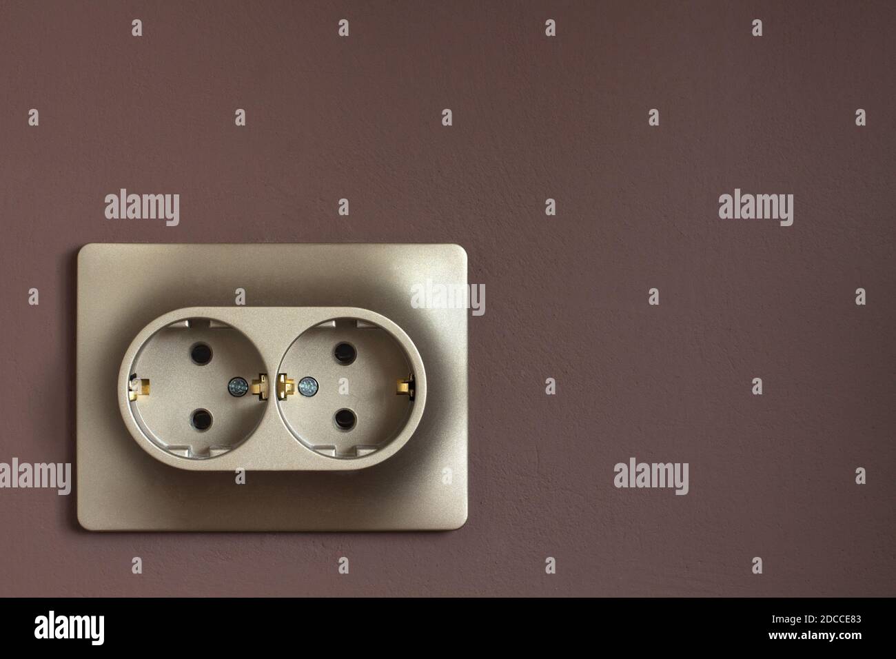 Goldene doppelte Steckdose an einer braunen Wand. Europäischer Standard-Elektrostecker in Nahaufnahme Stockfoto