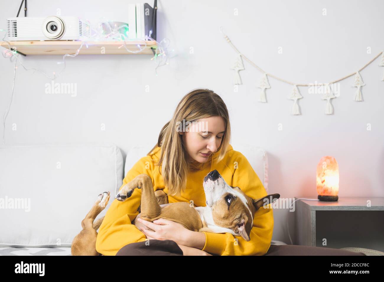 Junge Frau umarmt ihren Hund, Innenschlafzimmer Szene. Freude von Haustieren zu Hause oder während Aussperrung oder Selbstisolation, kalte Wintersaison Stockfoto