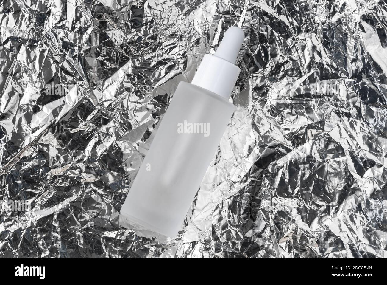 Serum mit Kollagen und Peptiden auf zerknitterter Silbermetallfolie. Hyaluronsäure-Öl-Tinktur auf faltiger Aluminiumtinktur. Beauty-Produkt Stockfoto