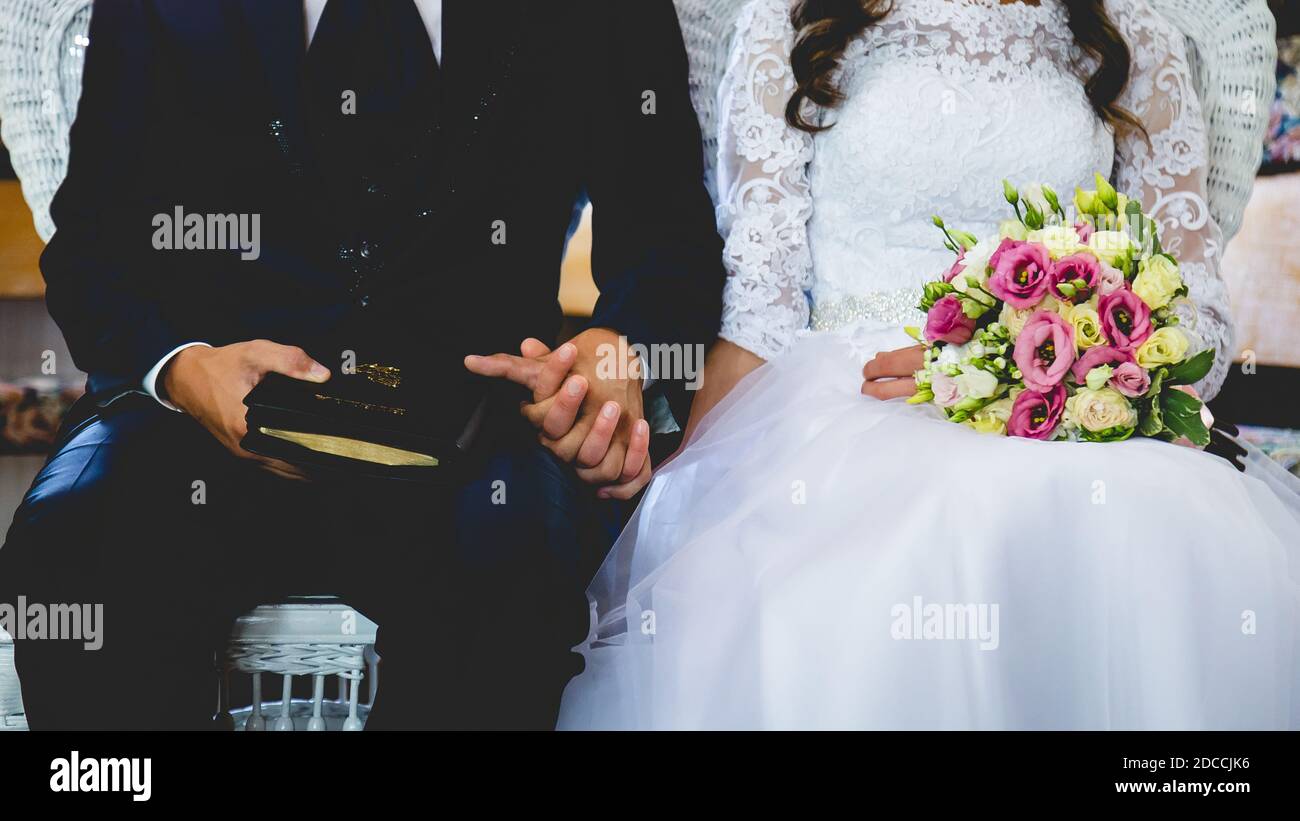 Nahaufnahme eines mittleren Teils einer Braut Mit einem bunten Blumenstrauß und Bräutigam, der sich hält Hände Stockfoto