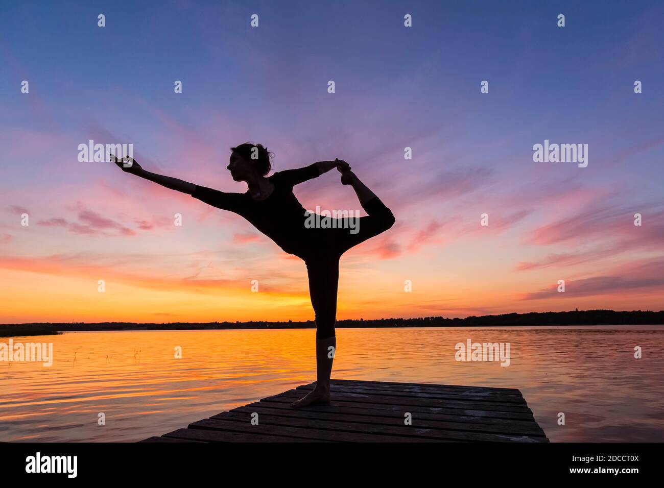 Frau praktiziert Yoga Haltung Natarajasana / Herr des Tanzes Pose, einbeinige stehend, balancieren, rückenbeugende Asana auf Steg am See bei Sonnenuntergang Stockfoto