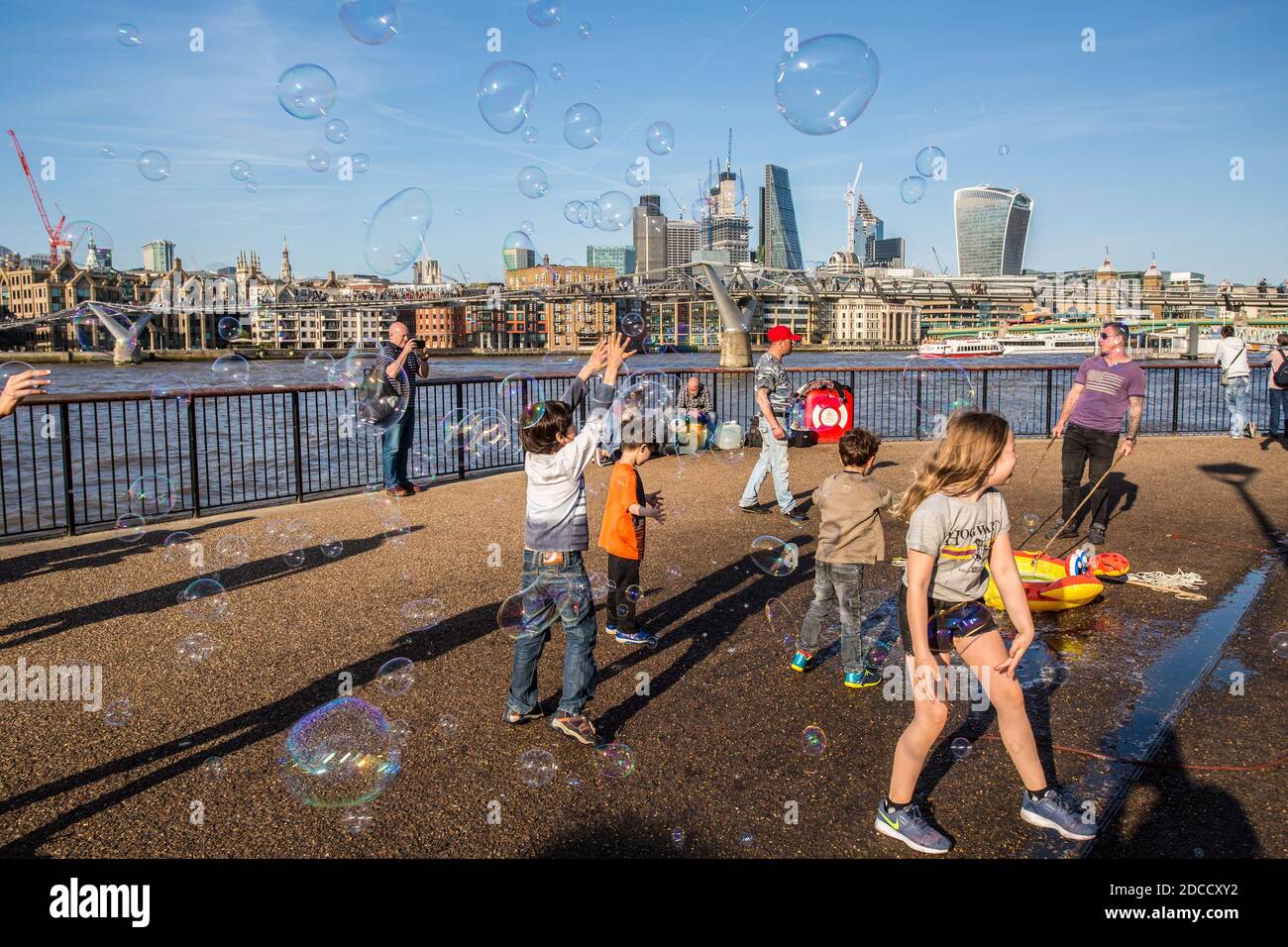 Kinder, die sich an einem heißen Sommertag mit Seifenblasen amüsieren, mit Blick über die Themse, auf die Skyline der Stadt London, London, Großbritannien. Stockfoto