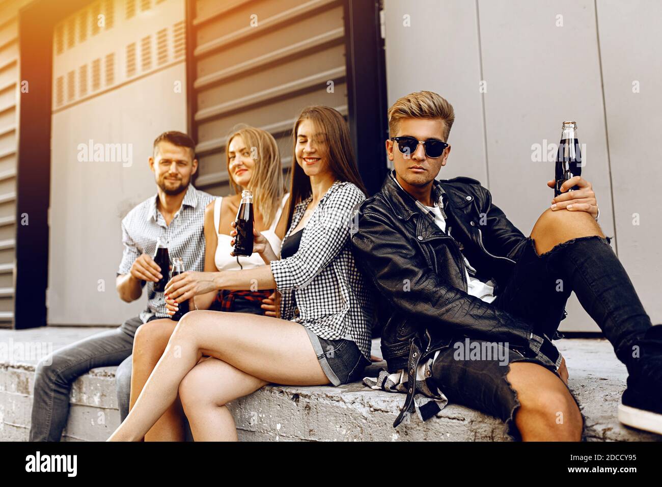 Stilvolle junge Freunde trinken Getränke in Glasflaschen, sitzen auf der Treppe Stockfoto