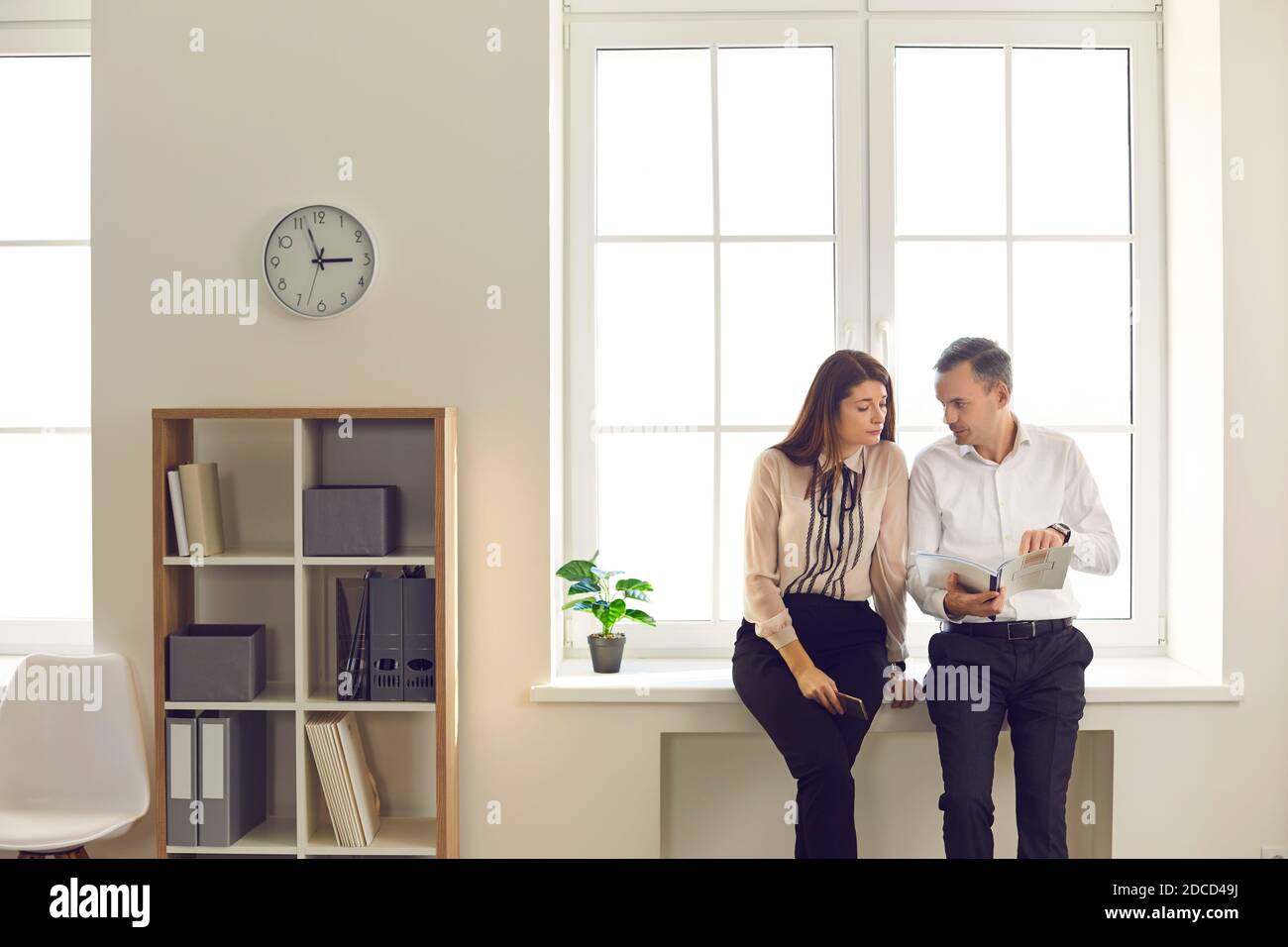 Mann und Frau Büroangestellte analysieren Dokumente, die im Büro am Fenster stehen. Stockfoto