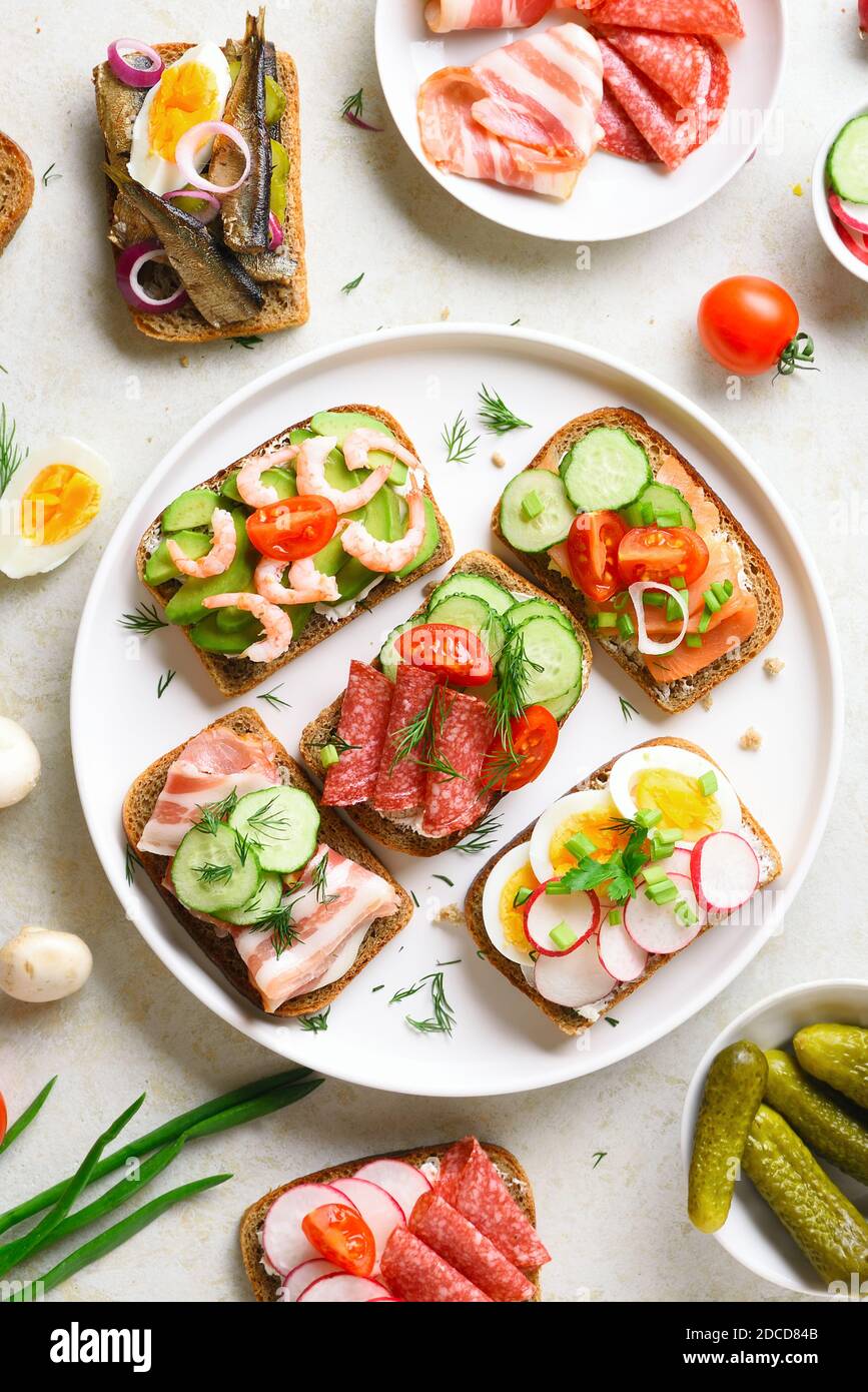 Offene Sandwiches mit Fleisch, Gemüse und Meeresfrüchten. Sortiment offene Sandwiches auf hellem Stein Hintergrund. Draufsicht, flach liegend. Stockfoto