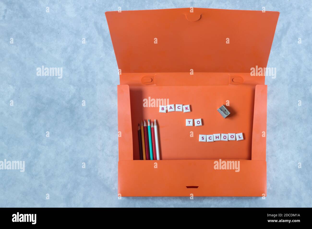 Eine Frontansicht von oben auf eine offene orangefarbene Mappe mit Buntstiften, einem Bleistiftspitzer, einem Mosaikbuchstabe mit dem Satz "zurück zur Schule". Stockfoto