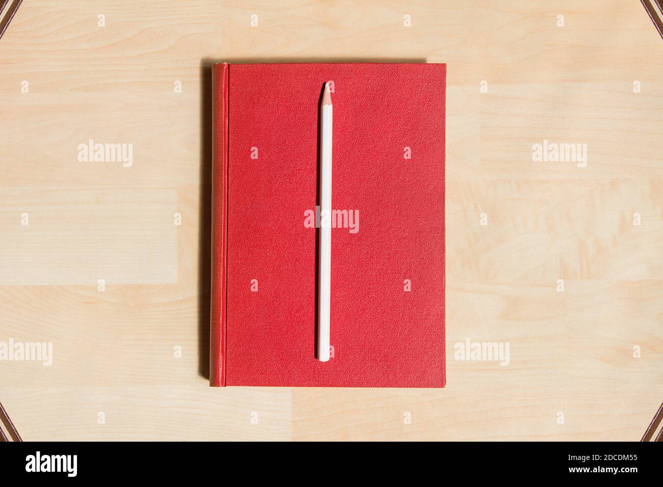 Weißer Bleistift in rotem Hardcover auf Parkett-Hintergrund und einige Bücher in den Ecken als Rahmen. Stockfoto