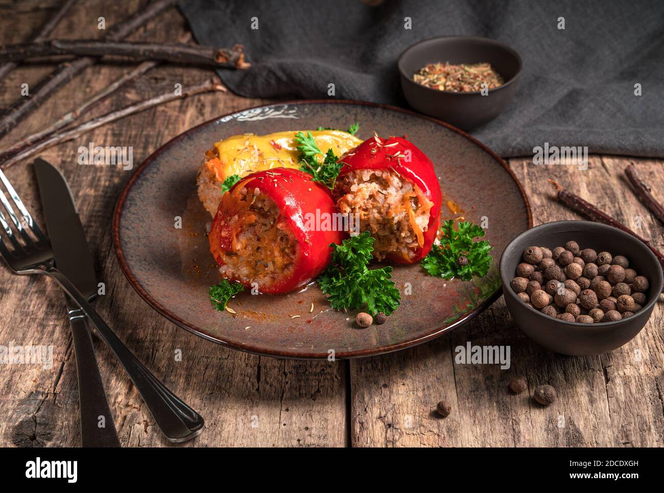 Pfeffer mit Hackfleisch auf einem braunen Teller, Gewürze und Besteck auf einem Holzhintergrund. Stockfoto