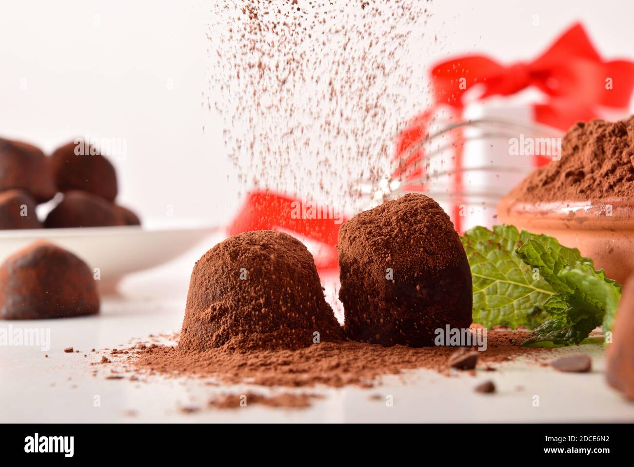 Kakaopulver fallen auf Schokolade Trüffel auf weiße Küchenbank für eine Veranstaltung und Geschenk im Hintergrund vorbereitet. Vorderansicht. Horizontale Zusammensetzung Stockfoto
