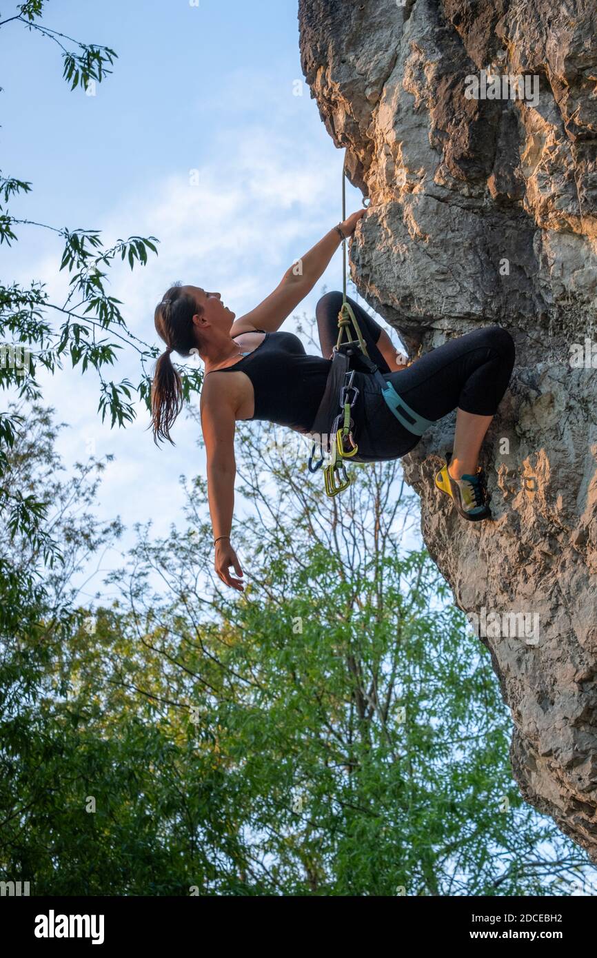 Glücklich schöne kaukasische Frau mit langen braunen Haaren aktiv Rock Klettern im Freien in einer schönen Landschaft zwischen grünen Bäumen und Klippen an einem sonnigen Tag Stockfoto