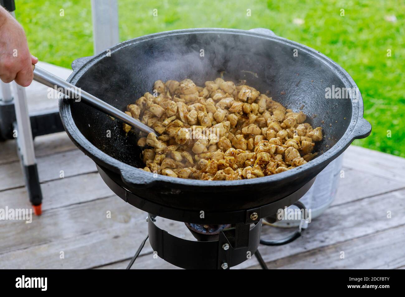 Mann, der Fleisch im gusseisernen Kessel im Freien röstet. Stockfoto