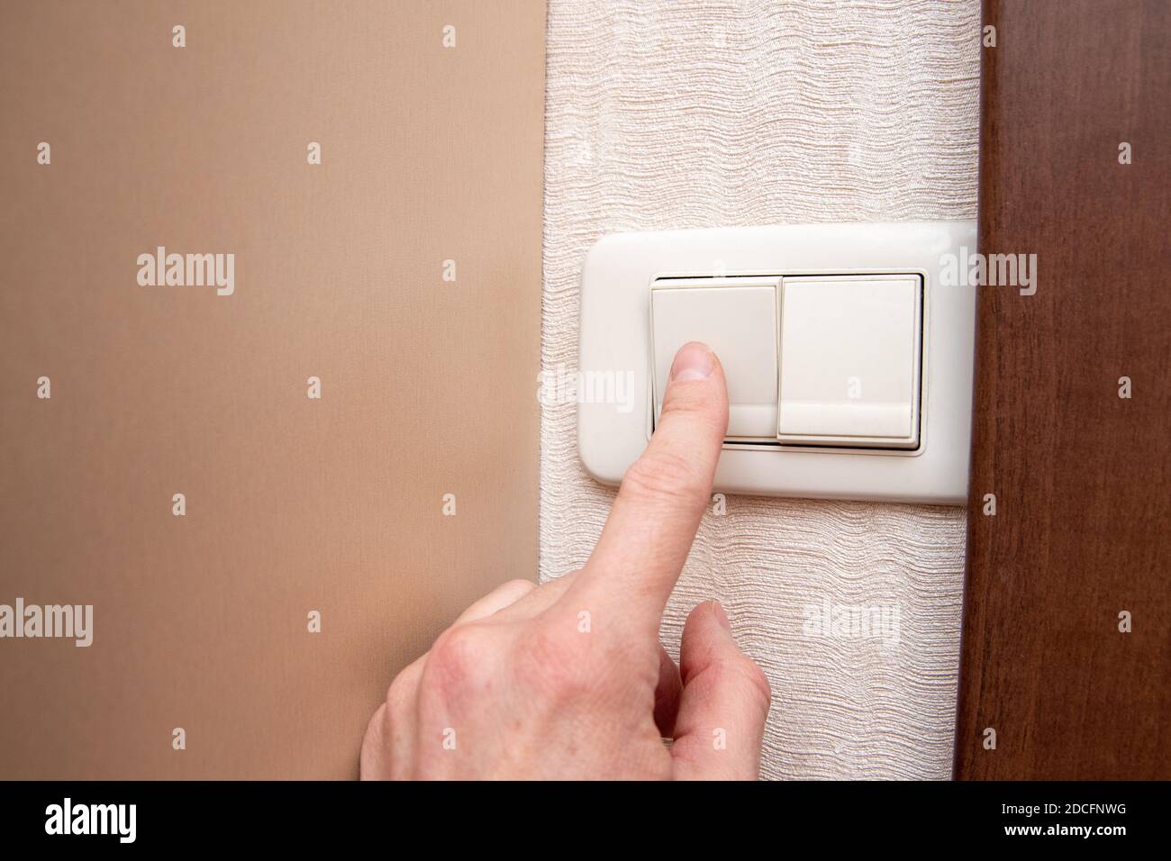 Nahaufnahme der Hand einer Frau, die das Licht mit einem Wandschalter ein- oder ausschaltet, Vorderansicht, Nahaufnahme, Kopierbereich. Energiesparkonzept Stockfoto