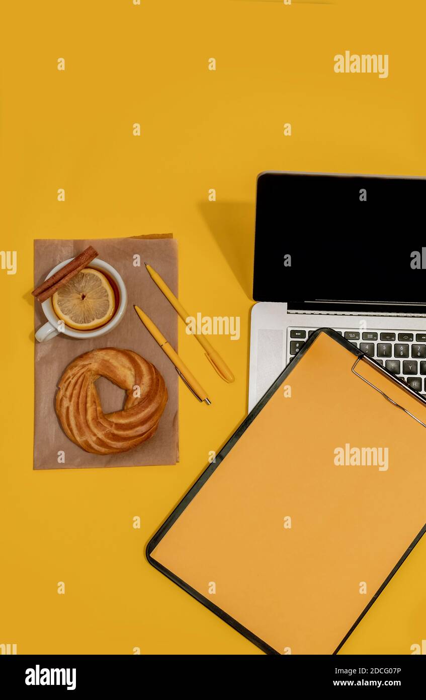 Laptop, Kuchen, Tasse Tee und Lebenslauf Blatt auf der Fortuna Gold Gelb Farbe Hintergrund, Draufsicht. Stockfoto