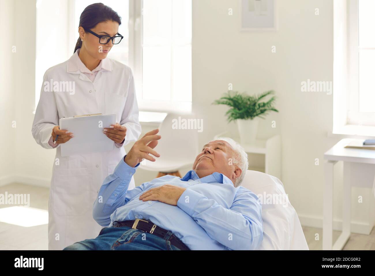 Arzt hört dem älteren Patienten zu, der über seine Symptome spricht und Krankengeschichte ausfüllen Stockfoto