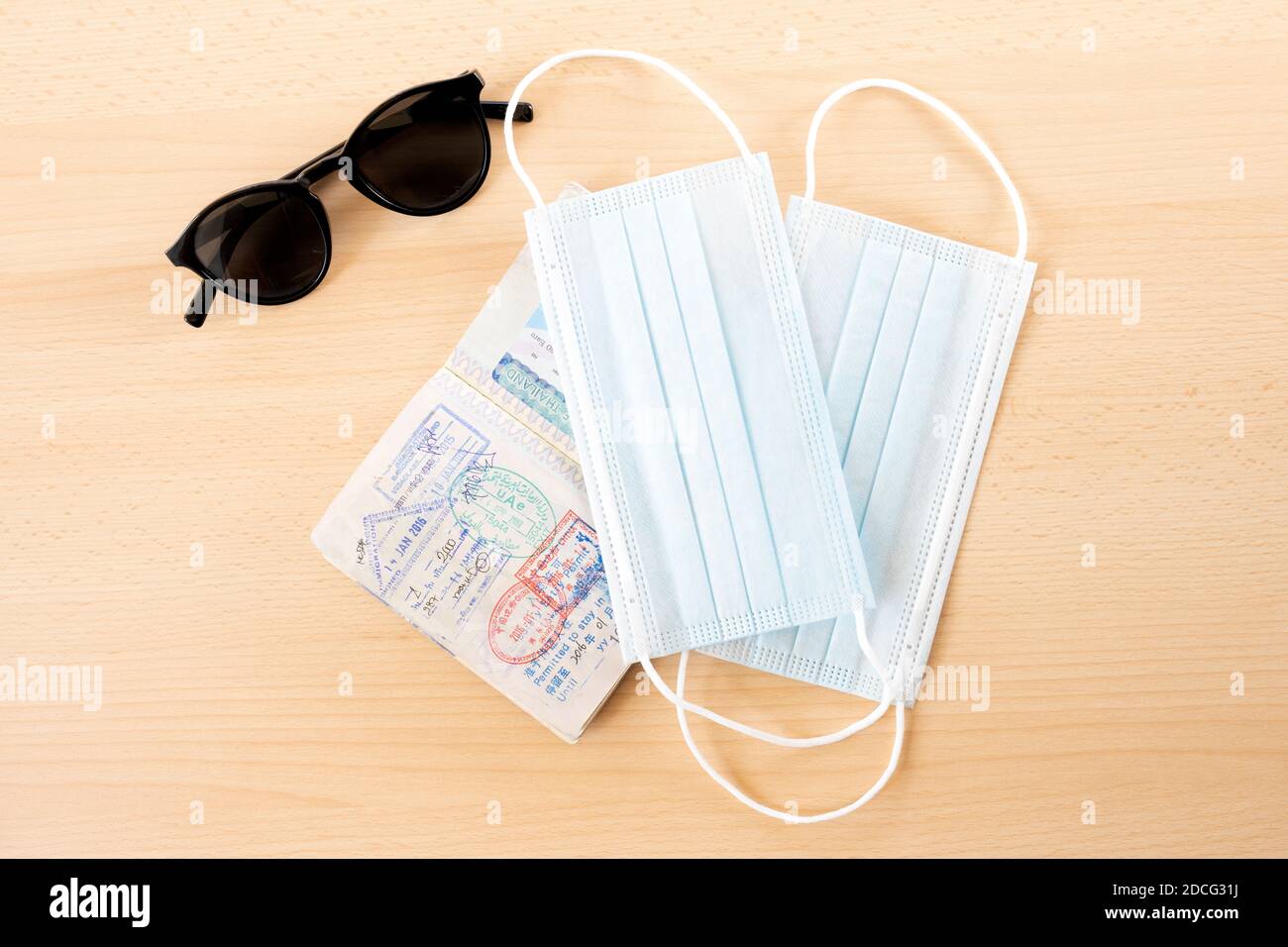 Sicheres Reisekonzept, Gesichtsmasken, Reisepass und Sonnenbrille sind auf einem Holztisch angeordnet. Stockfoto