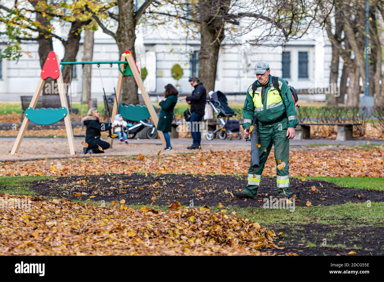 Riga, Lettland - 6. November 2020: Ein Arbeiter mit Gebläse reinigt einen Stadtpark und bläst Herbstblätter weg Stockfoto