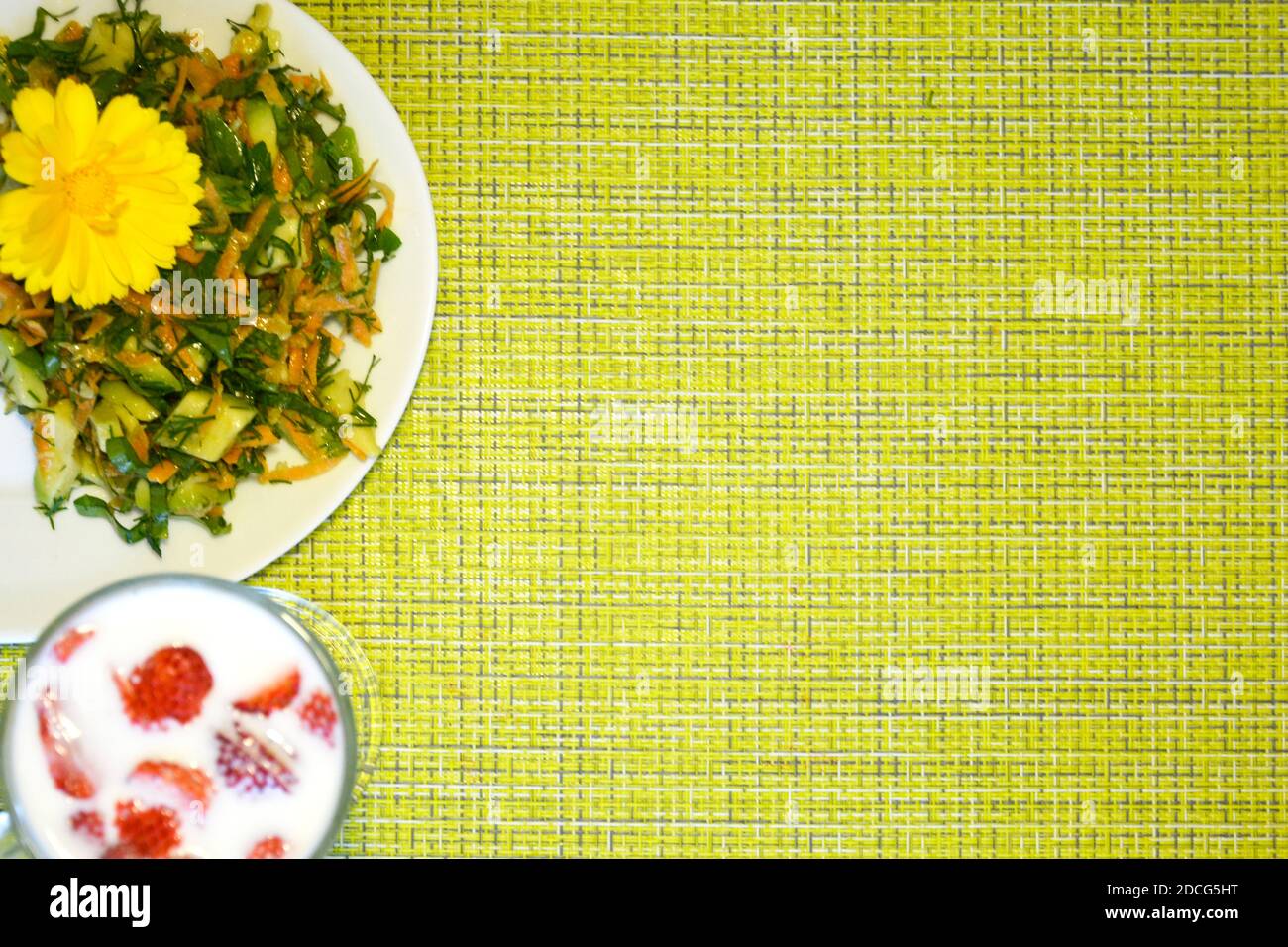 Grüner Hintergrund mit Teller und Platz für Text. Salat mit Kapuzinerkresse und einem Glas Milch und Erdbeeren auf einer Serviette. Stockfoto