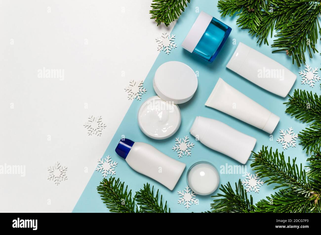 Set von Winter Hautpflege Kosmetik-Produkte auf weißem und blauem Hintergrund mit Tannenzweigen. Cremedose, Tube, Körperlotion, Milch und Reinigungsflasche Stockfoto