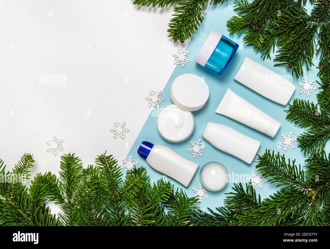 Set von Winter Hautpflege Kosmetik-Produkte auf weißem und blauem Hintergrund mit Tannenzweigen. Cremedose, Tube, Körperlotion, Milch und Reinigungsflasche Stockfoto