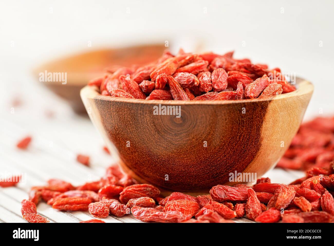 Getrocknete Goji-Beeren in einer kleinen Holzschüssel, einige über weißen Brettern Tisch unter verstreut Stockfoto
