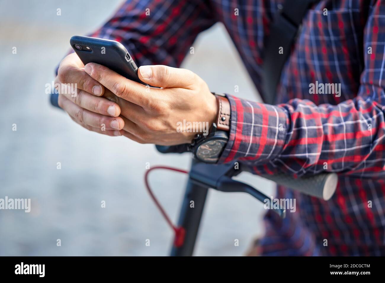 Junger Mann trägt Hemd auf Elektroroller Lenker lehnt, hält Handy in den Händen, Nahaufnahme Detail Stockfoto