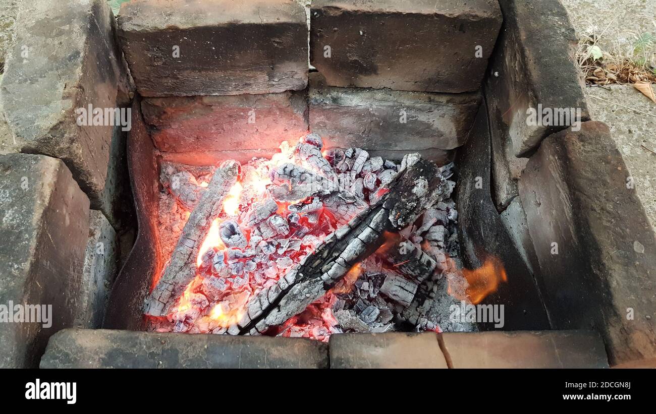 Verbrannte Holzstämme mit schwelender Flamme auf schwarzer rissiger Holzoberfläche. Bonfire-Texturen. Picknick-Lagerfeuer zum Kochen von Essen am offenen Feuer. Camping Conce Stockfoto