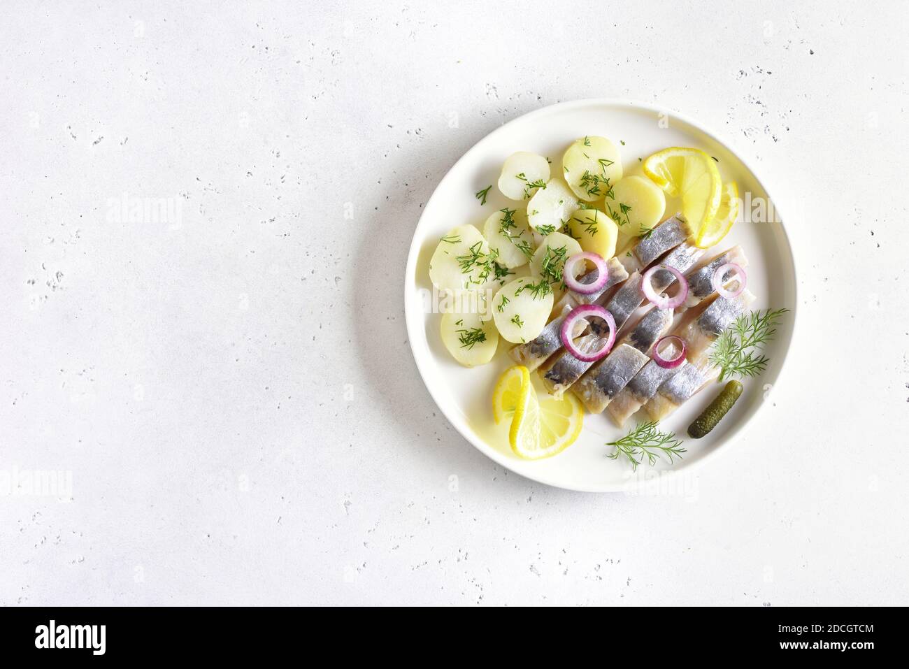 In Scheiben geschnittener Heringfisch mit gekochten Kartoffeln auf weißem Teller auf hellem Steinhintergrund mit freiem Textraum. Russische Küche. Draufsicht, flach liegend Stockfoto