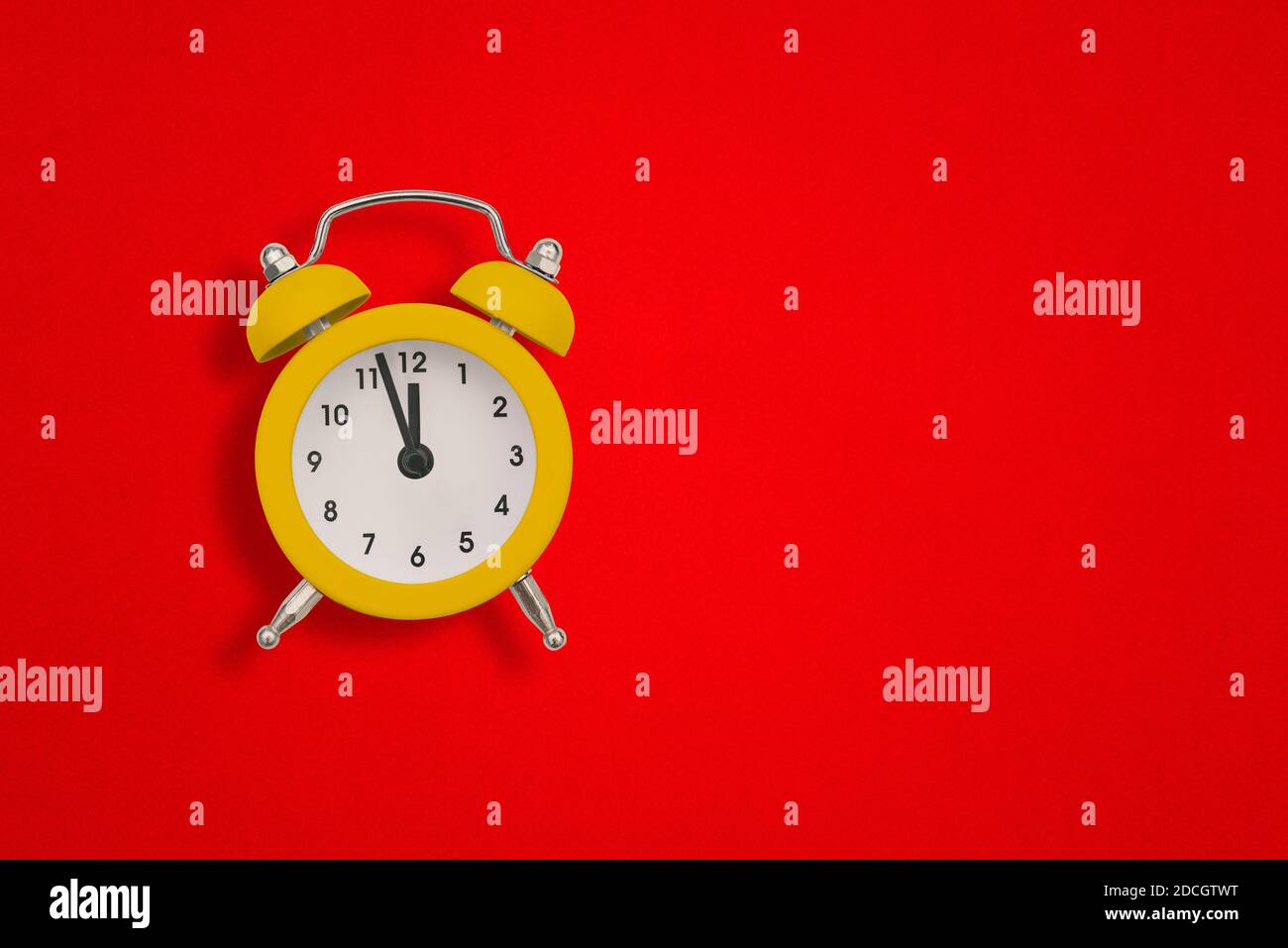 Gelber Wecker auf rotem Papier mit Kopierplatz. Die Zeiger der Uhr zeigen zwölf Uhr. Stockfoto
