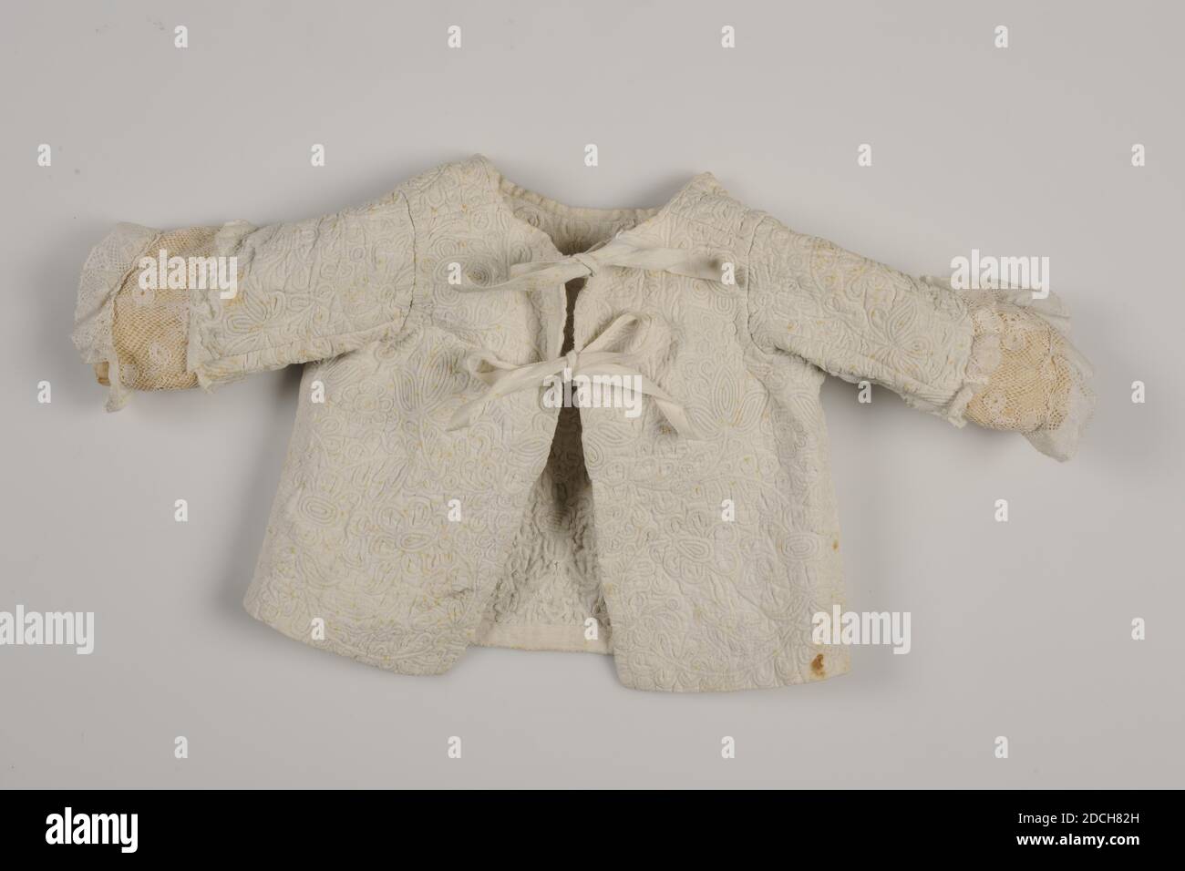 Mantel, Anonymous, letztes Viertel des 18. Jahrhunderts, Spitze, Leinen, Seide, Allgemein leicht gepolstert: 21 x 40 x 4.5cm 210 x 400 x 45mm, Weiße Babyjacke aus Leinen von Zaans mit Pflanzen- und Blumenmotiven. Die Jacke schließt in der Mitte vorne mit zwei Bändern. Es hat lange Set-in-Ärmel mit einem gelben Seidenärmelbezug mit einem Streifen aus Spitze genäht darüber. Die Spitze ist entlang der Ärmelenden gefräst. Die Nähte sind auf der Innenseite mit einem Leinenband, Blume geschnitten Stockfoto