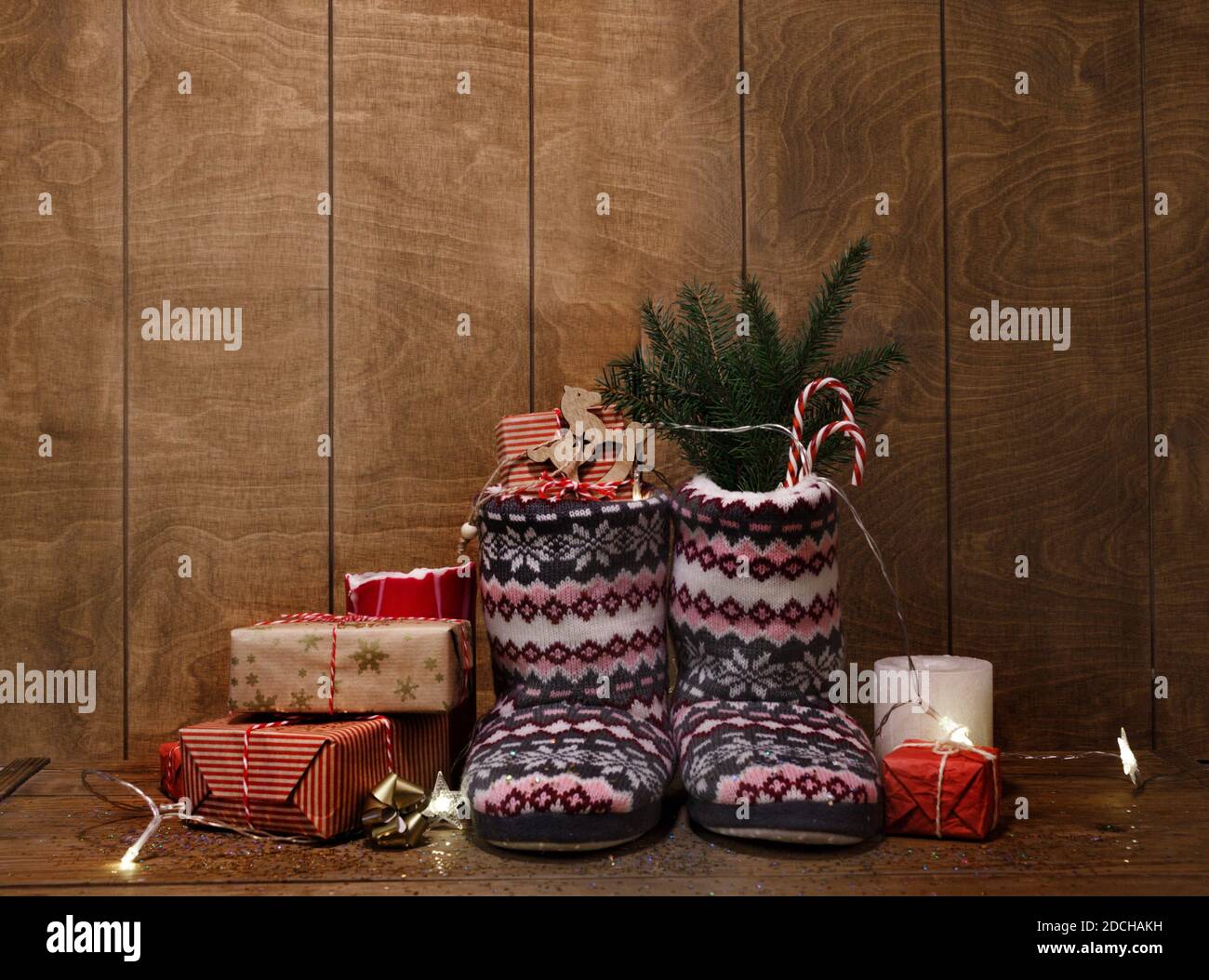 Gestrickte Weihnachtsstiefel auf Holzhintergrund zwischen Geschenken und Kerzen. Stockfoto