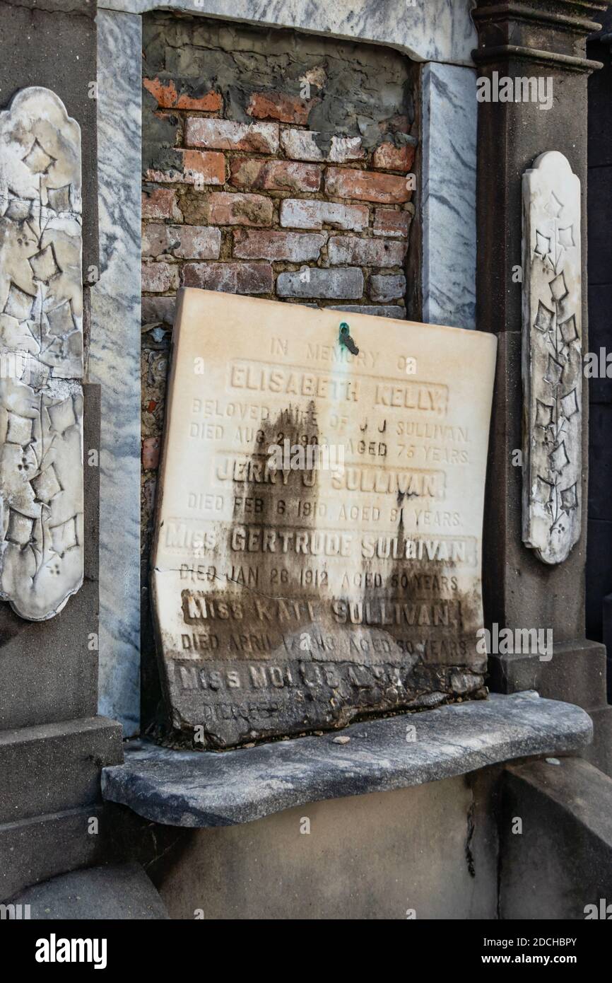 Ein alter, verwitterter Grabstein mit eingravierten Namen und Daten, der an einer sich verschlechternden Backsteinmauer des Friedhofs in New Orleans, Louisiana, befestigt ist Stockfoto
