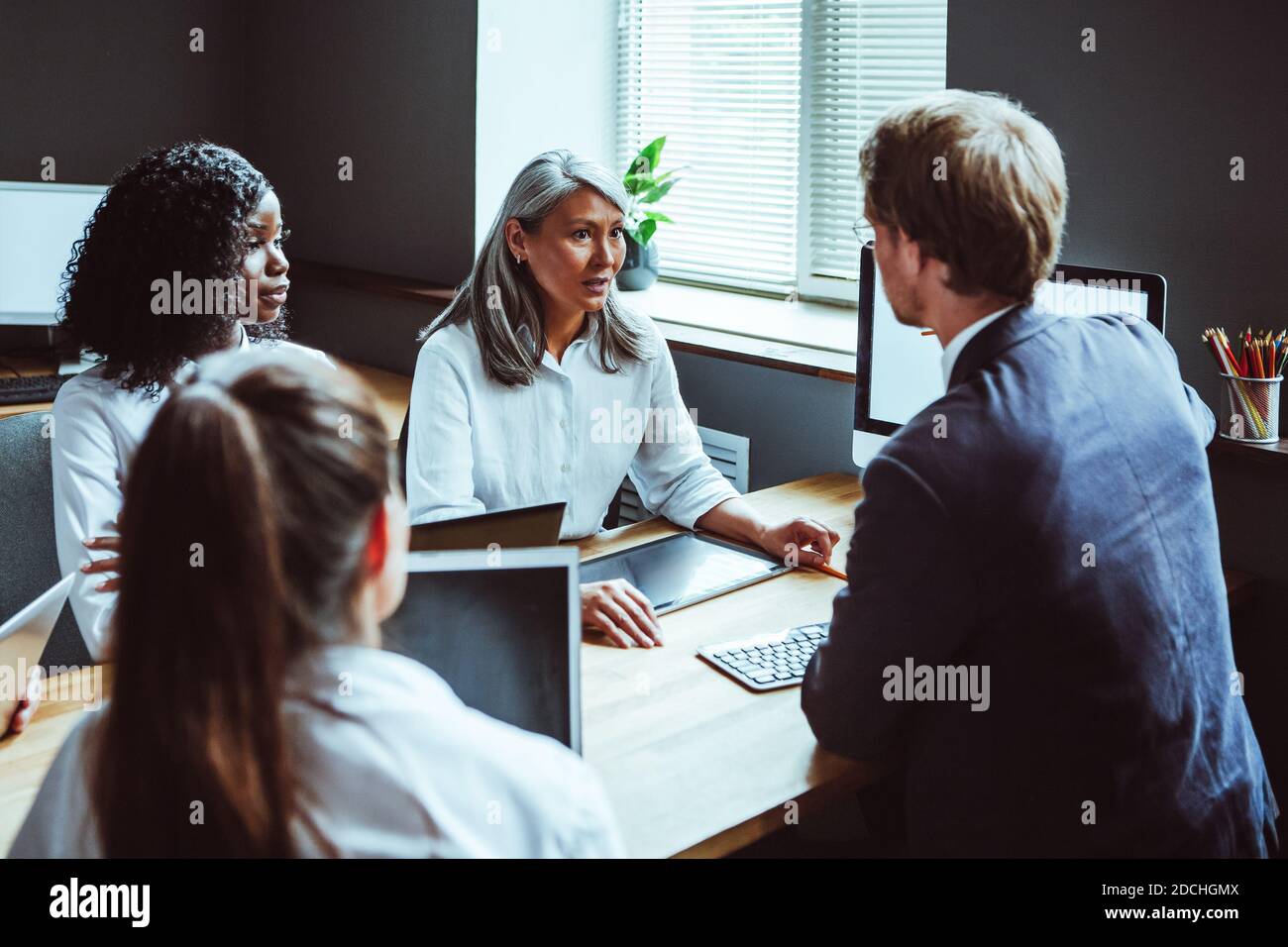 Multiethnisches Geschäftsteam mit Computern bei der Besprechung. Hände von Geschäftsleuten berühren Bildschirm des elektronischen Geräts. Getöntes Bild. Seitenansicht Stockfoto