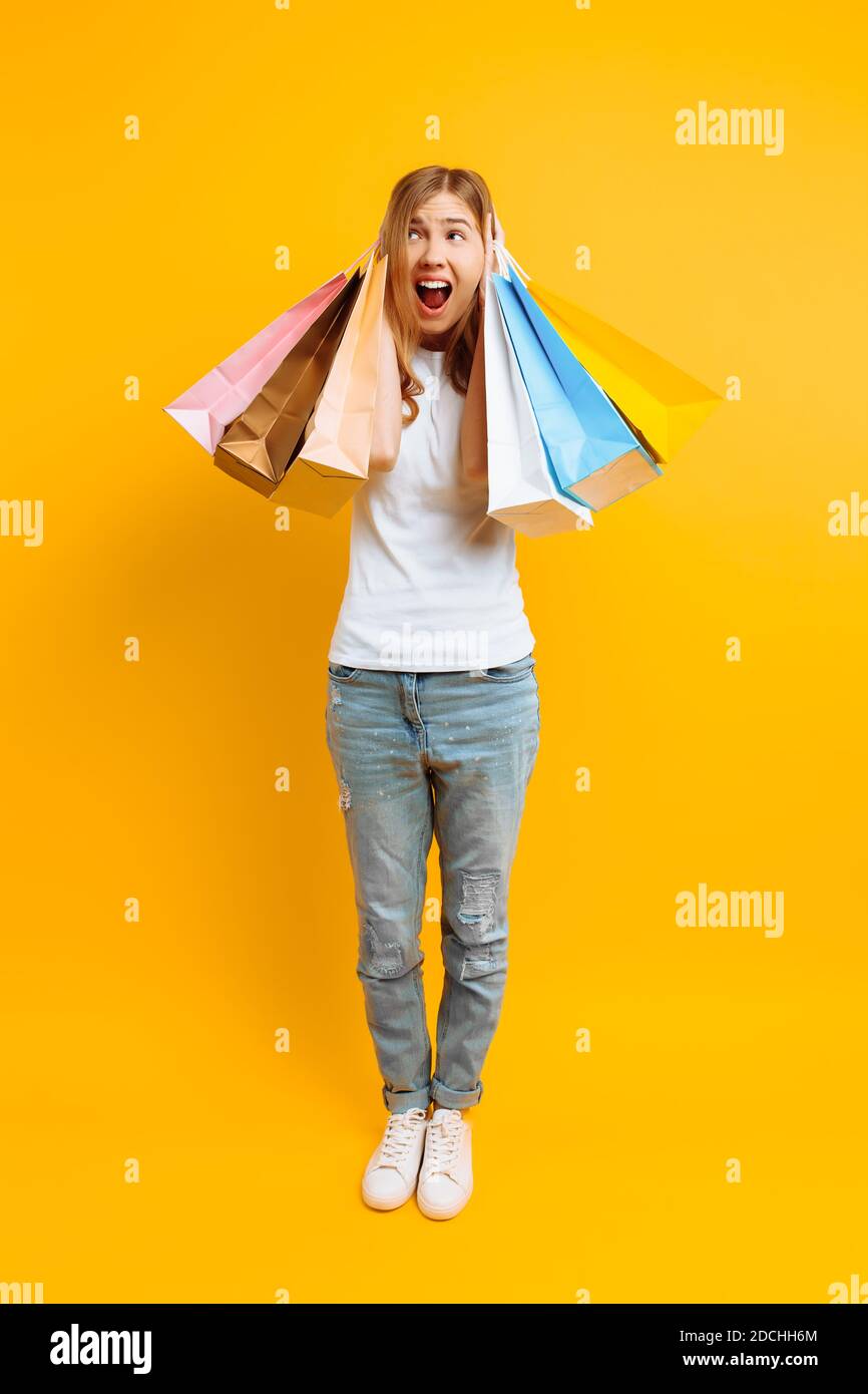 In voller Länge verärgert Mädchen Gefühl müde vom Einkaufen, Frau mit vielen Taschen, schönes Mädchen mit Taschen auf gelbem Hintergrund Stockfoto