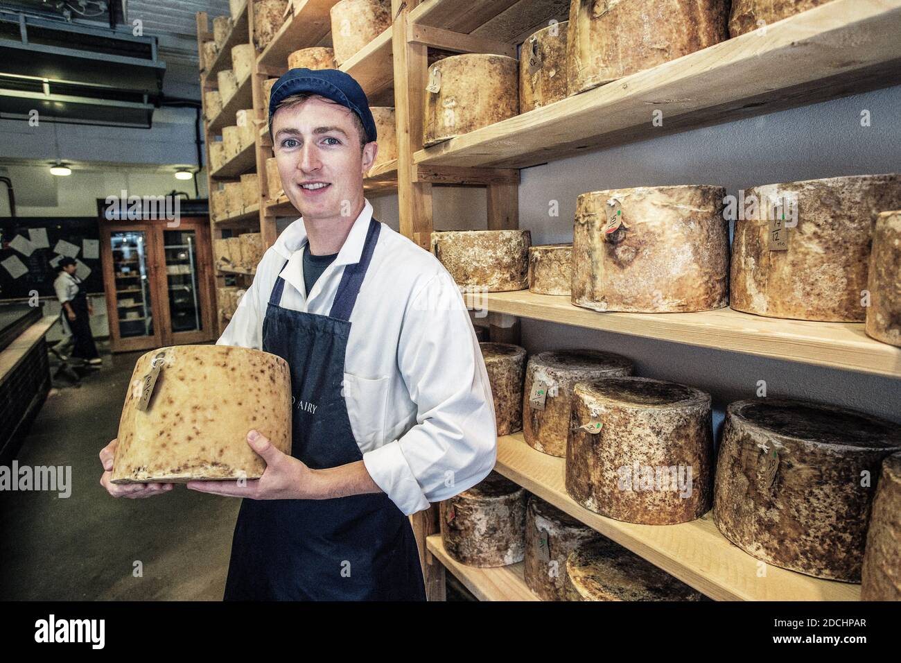 Junger Mann, der einen großen Käse in der Neal s Yard Dairy auf dem Borough Market in Southwark, London, England, hält. Stockfoto