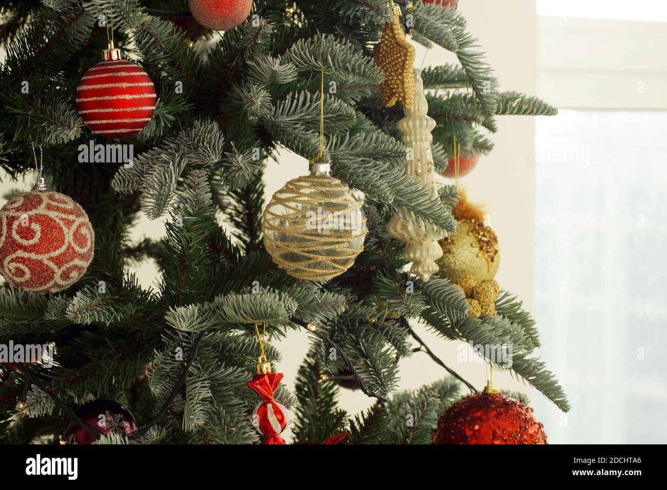 Weihnachtsschmuck auf einem Baum im Haus. Rote und goldene Weihnachtsdekorationen hängen vom Baum. Stockfoto