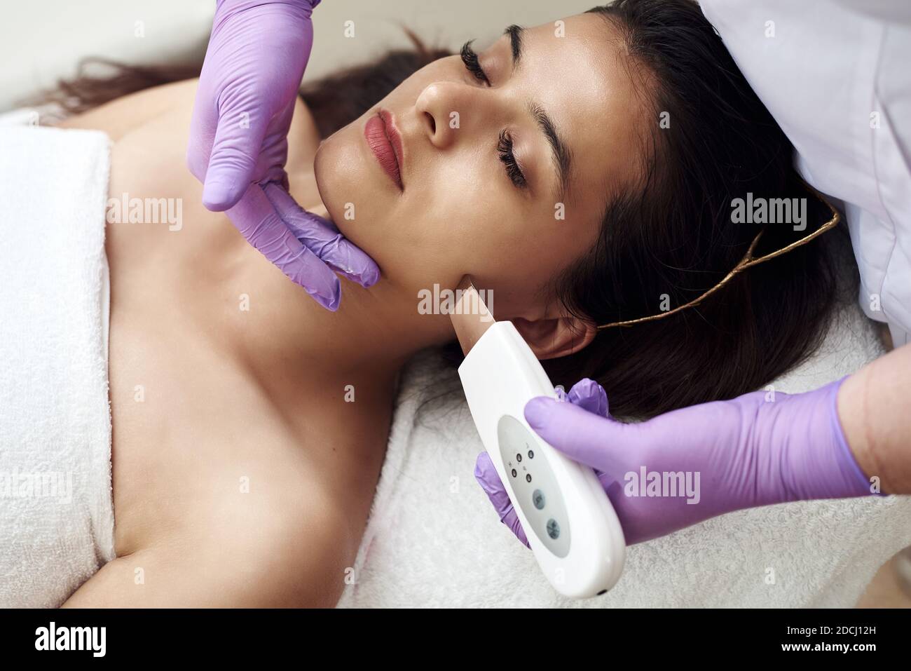 Eine Frau macht eine Ultraschallreinigung des Gesichts und der Haut zu einem Klienten. Moderne Ausstattung. Junge hübsche Frau, die Behandlungen in Schönheitssalons erhält und auf der Couch liegt. Stockfoto