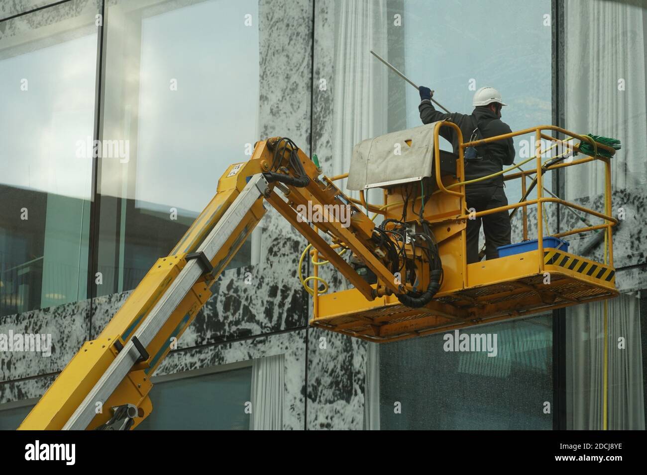 Wallisellen, Schweiz - 05 28 2020: Ein Mann, der große Fenster und Fassade eines hohen Firmengebäudes mit einem Mopp wäscht, steht auf einer hohen Plattform. Stockfoto