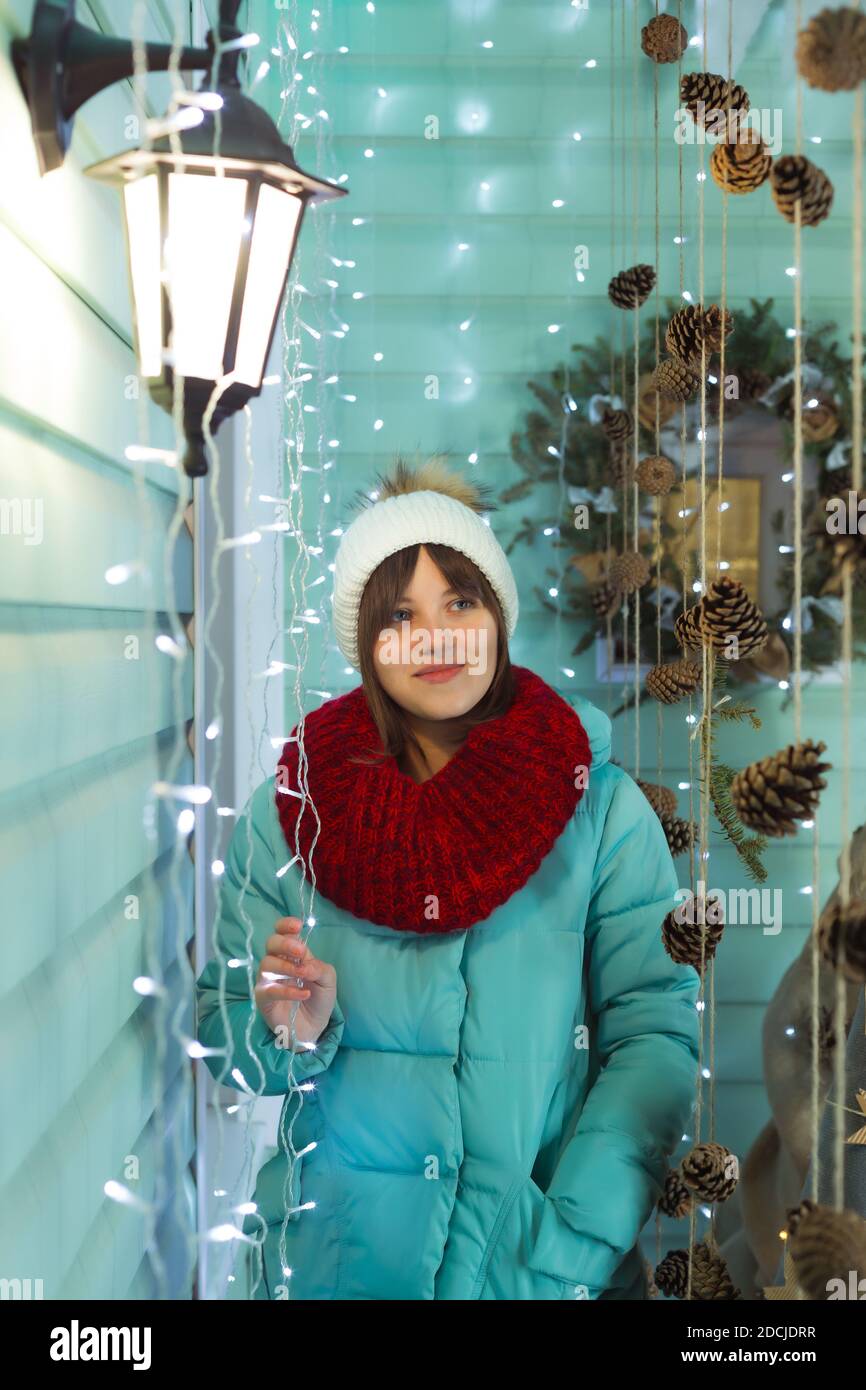 Junge Frau in einem warmen Hut, Schal und Daunenjacke auf dem Hintergrund der Weihnachtsdekoration Stockfoto