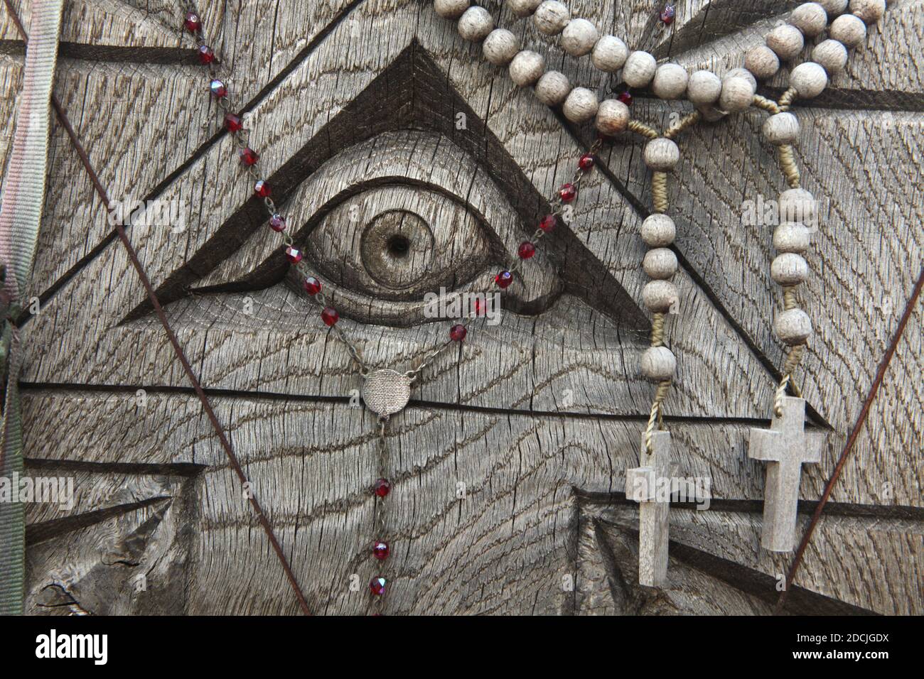 Das Auge der Vorsehung in dem mit Rosenkranz geschmückten Holzrelief auf dem Kreuzberg bei Šiauliai in Litauen. Der wichtigste litauische Wallfahrtsort befindet sich etwa 12 km von der Stadt Šiauliai entfernt. Niemand hat jemals versucht zu zählen, wie viele große und kleine Kreuze tatsächlich auf dem Hügel installiert sind, aber es wird angenommen, dass es hier mindestens zweihunderttausend Kreuze gibt. Und jeden Tag werden Dutzende oder sogar Hunderte von neuen Kreuzen von Pilgern aus der ganzen Welt hinzugefügt. Stockfoto