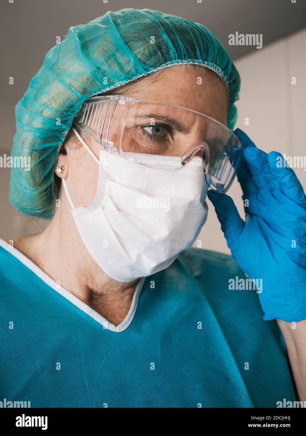 Portrait Gesundheitswesen professionelle Frau mit Schutz gegen covid 19 mit Handschuhe und Haarmütze setzen ihre Maske und Brille Stockfoto