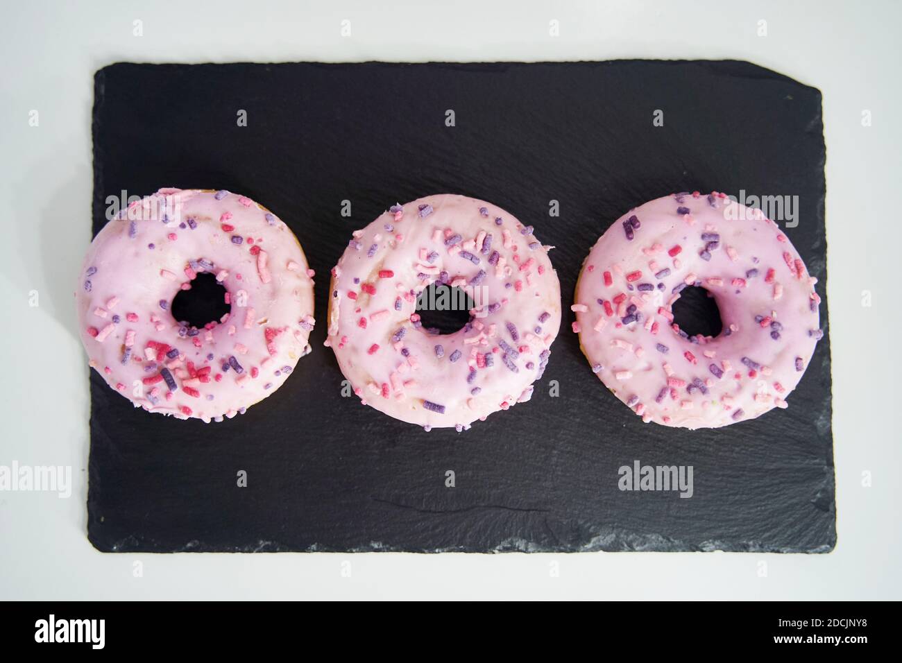 Süße glasierte rosa Donuts Nahaufnahme auf einem schwarzen Tablett Stockfoto